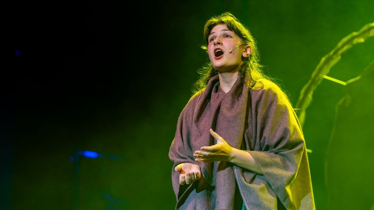 Young performer singing under green stage lighting